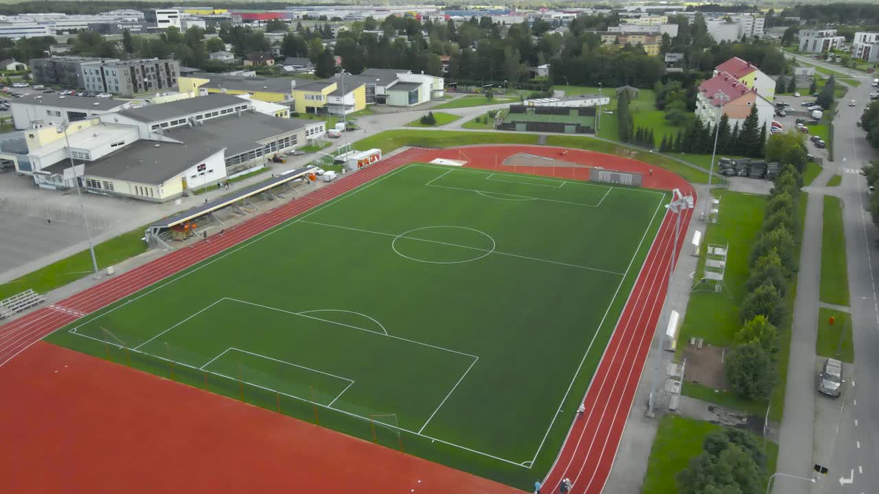 Aerial view of a modern freshly built and renovated soccer stadium or football field during a summer day, workers are creating new white lines on the running tracks around the grassy green stadium