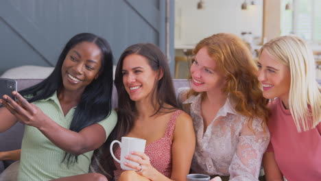 multi-cultural group of female friends sitting on sofa at home posing for selfie together