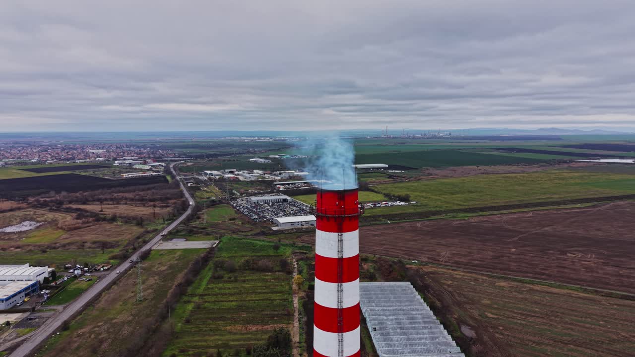 Il fumo si alza da un'alta ciminiera in una zona industriale vicino ai campi