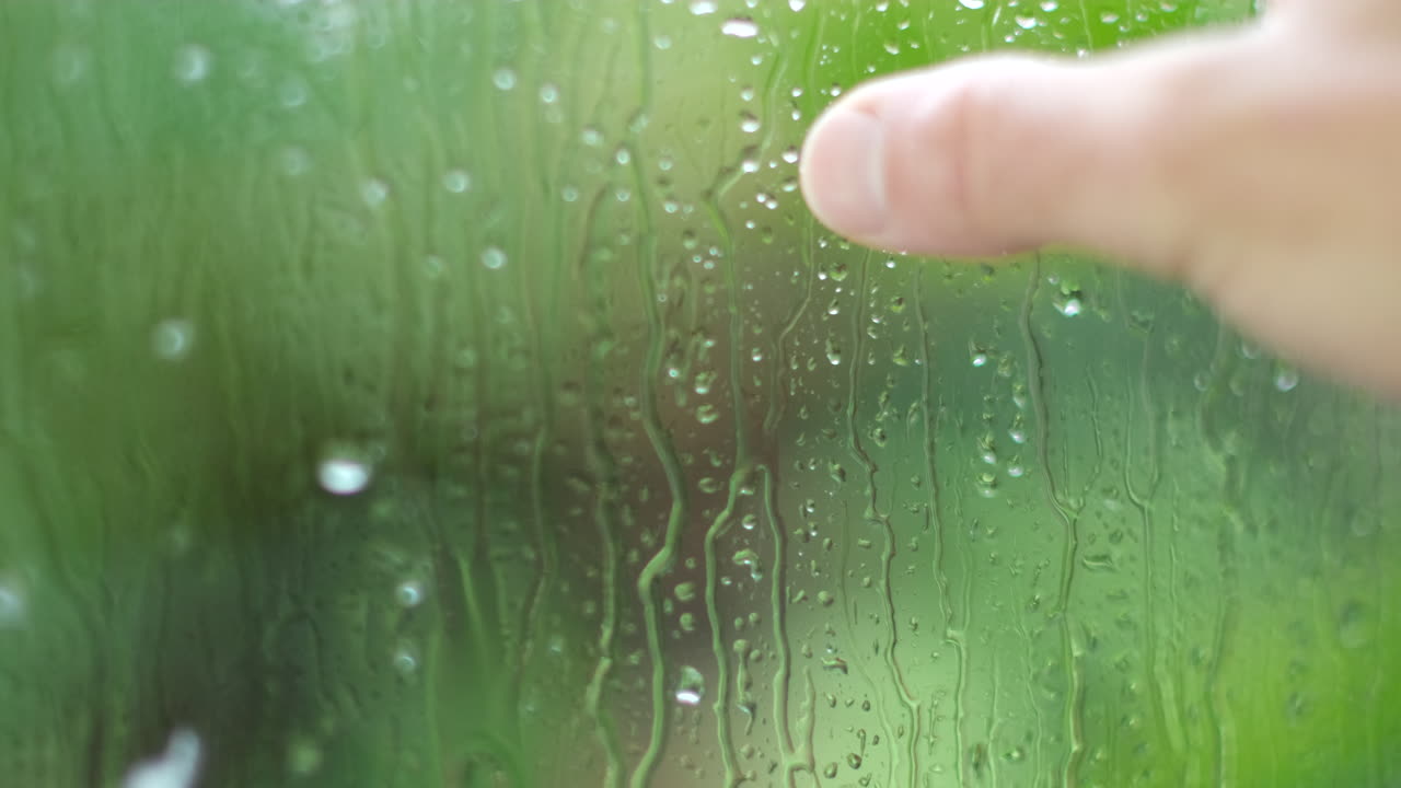 Fingers dragged over cold window indoors as it rains outside, nostalgia concept