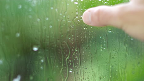 fingers dragged over cold window indoors as it rains outside, nostalgia concept