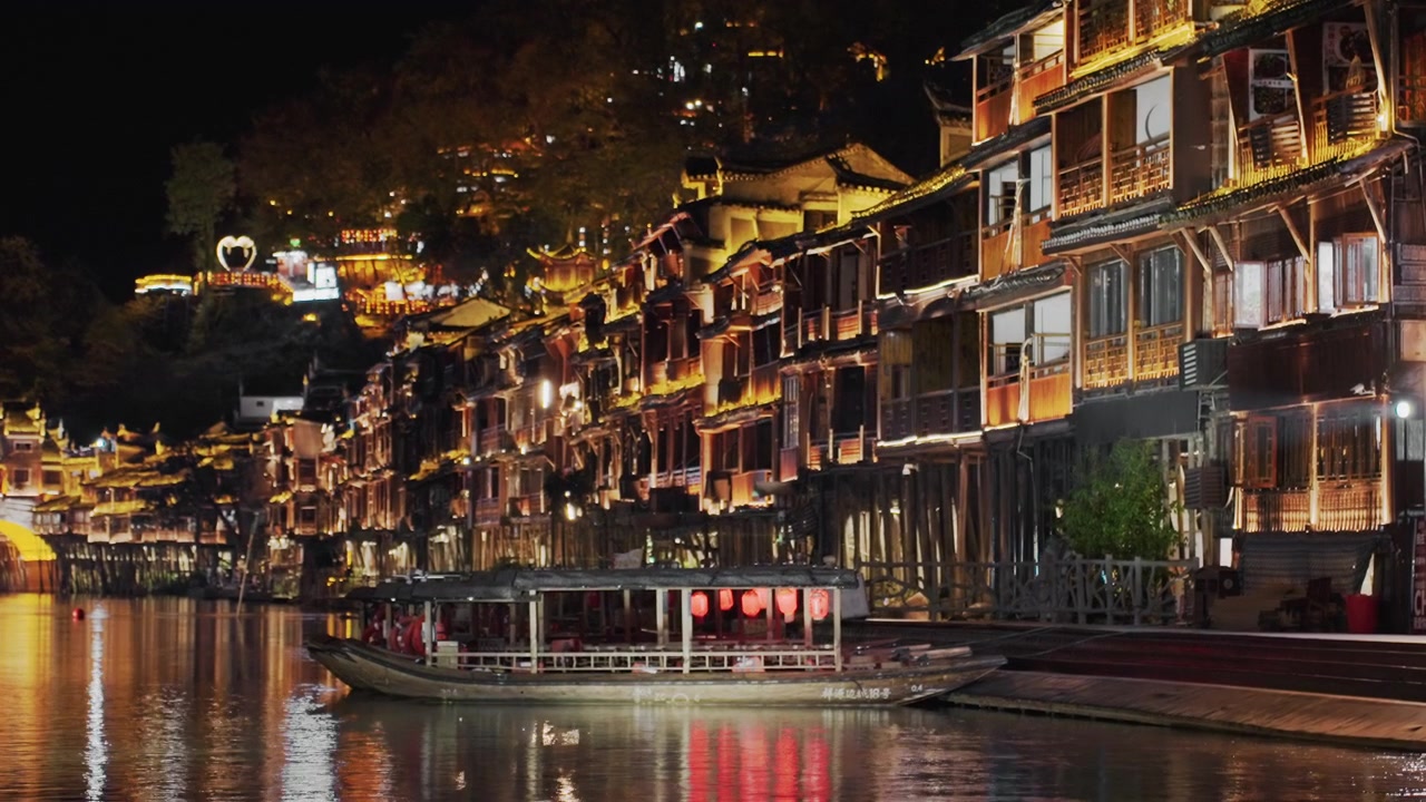 Orla noturna iluminada, com edifícios ribeirinhos de vários andares adornados com janelas brilhantes e lanternas nas varandas, um barco atracado projetando reflexos cintilantes, cafés e esplanadas aconchegantes, e um ambiente movimentado