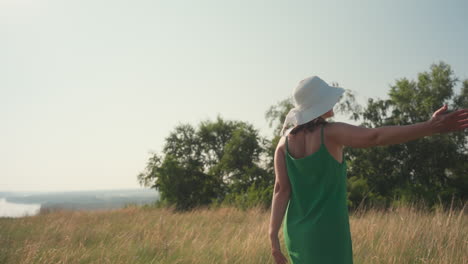 joyful young lady in green dress with wide smile dancing freely in golden field under clear blue sky during peaceful summer adventure with long dry grass swaying and distant trees at horizon