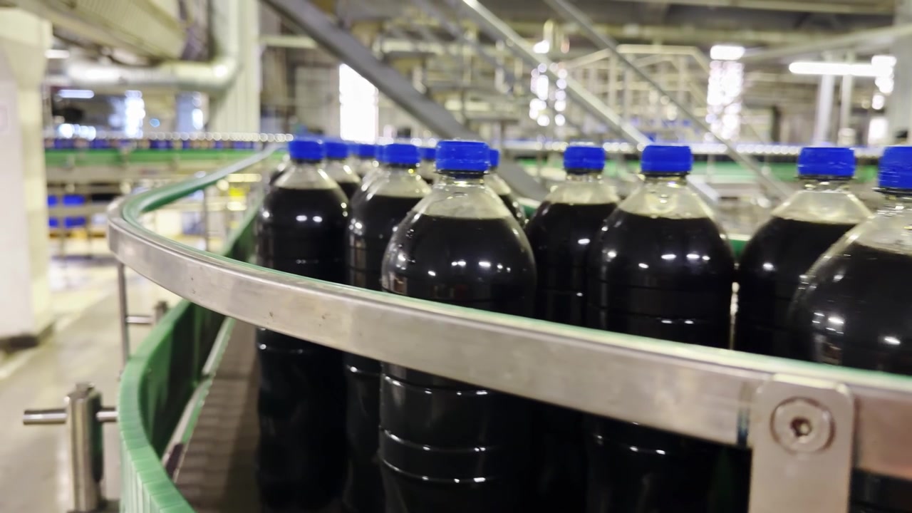 Visão detalhada de garrafas de refrigerante em esteira transportadora de fábrica automatizada.