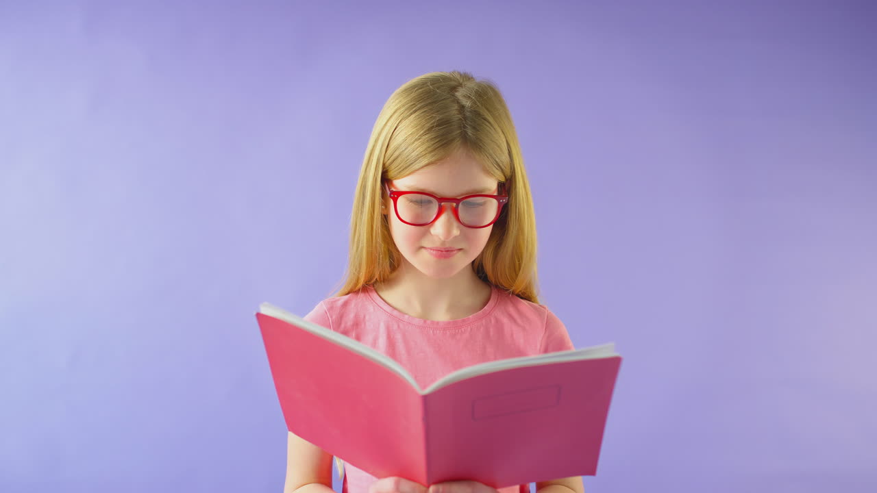 Scatto in studio di giovane ragazza con gli occhiali che studia un quaderno di scuola su sfondo viola.