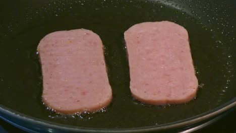 spam sizzling in a frying pan cooking a high cholesterol english breakfast unhealthy eating