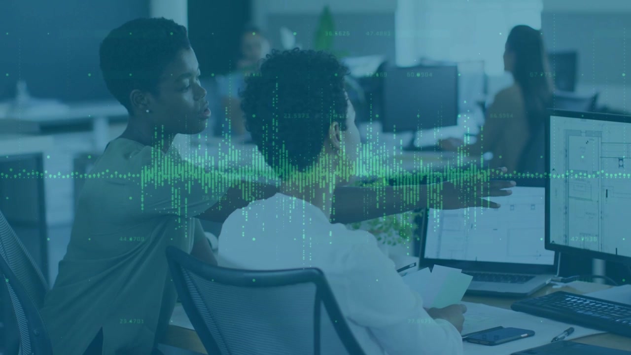 Two women working, one leaning and pointing, other typing, green waveform overlaying business data