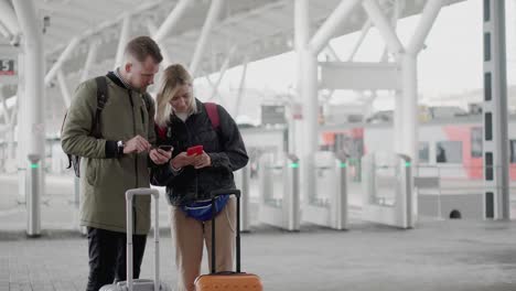 dos pasajeros están usando teléfonos inteligentes, de pie en la plataforma de la estación de tren