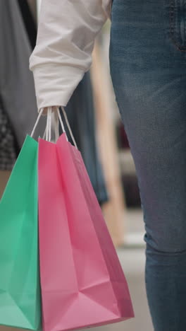 mujer compradora caminando con confianza en una tienda de ropa al por menor, con bolsas de compras rosas y verdes brillantes en la mano, con pantalones vaqueros casuales y una sudadera blanca