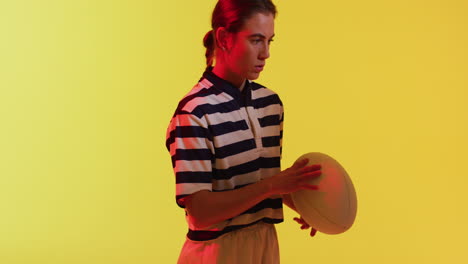 retrato de una jugadora de rugby caucásica con una pelota de rugby sobre iluminación amarilla de neón