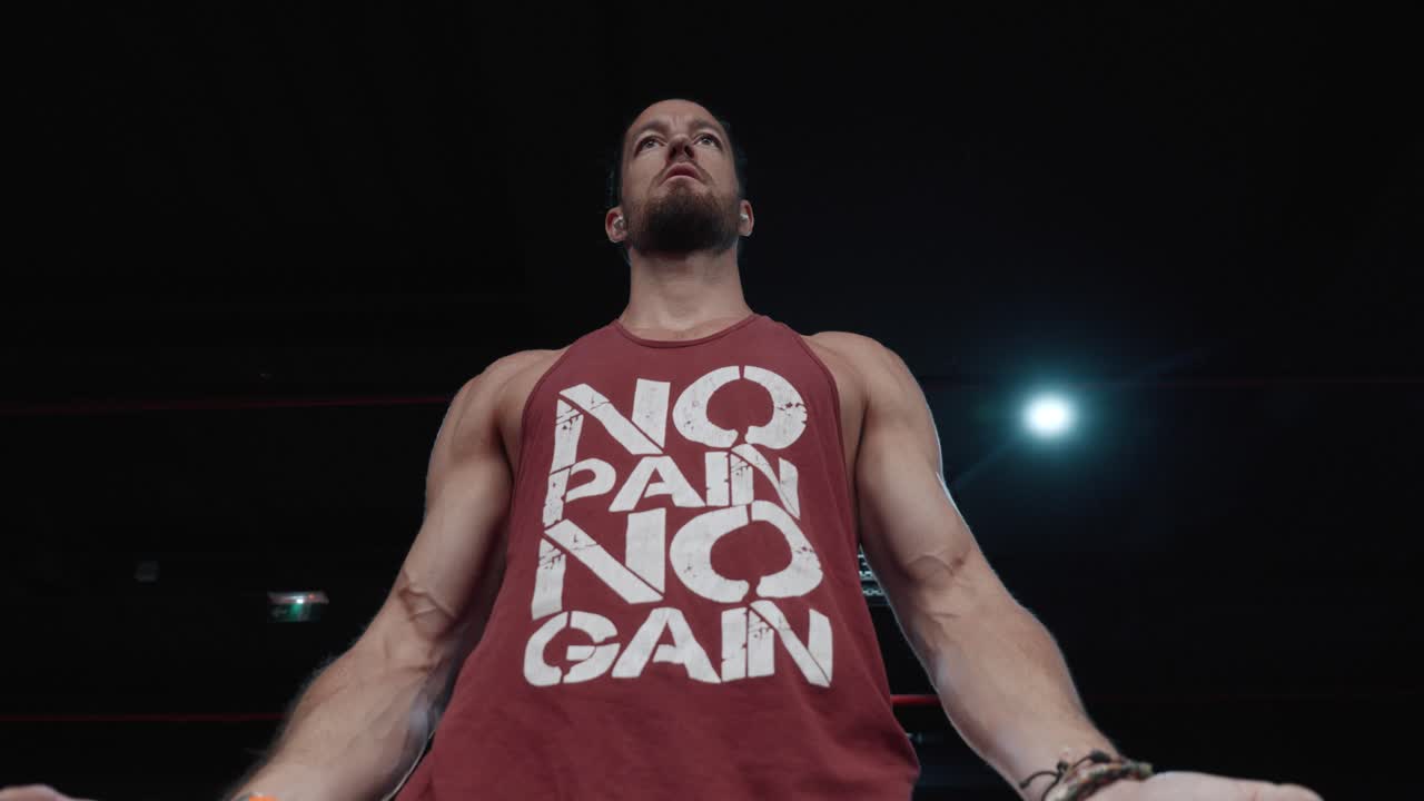 Plano a contrapicado de un culturista haciendo curls de bíceps controlados con barra