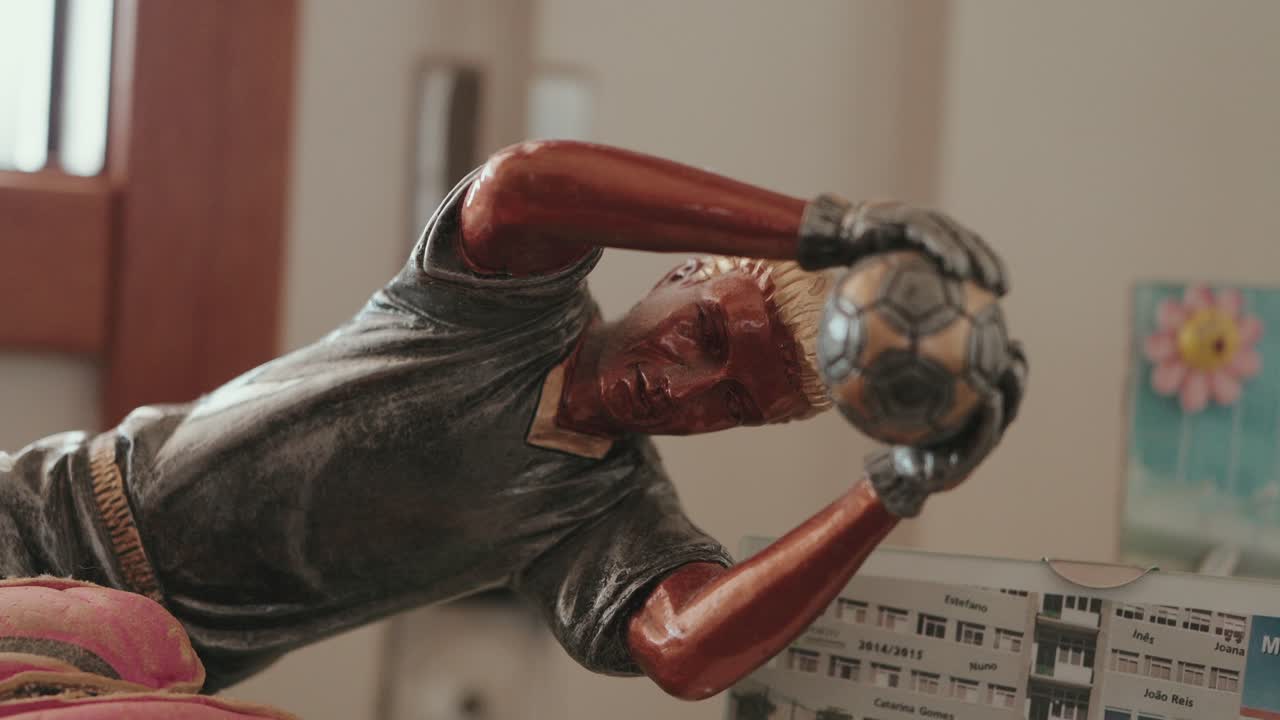 Close up of a metallic goalkeeper figurine mid-dive catching a soccer ball with both hands