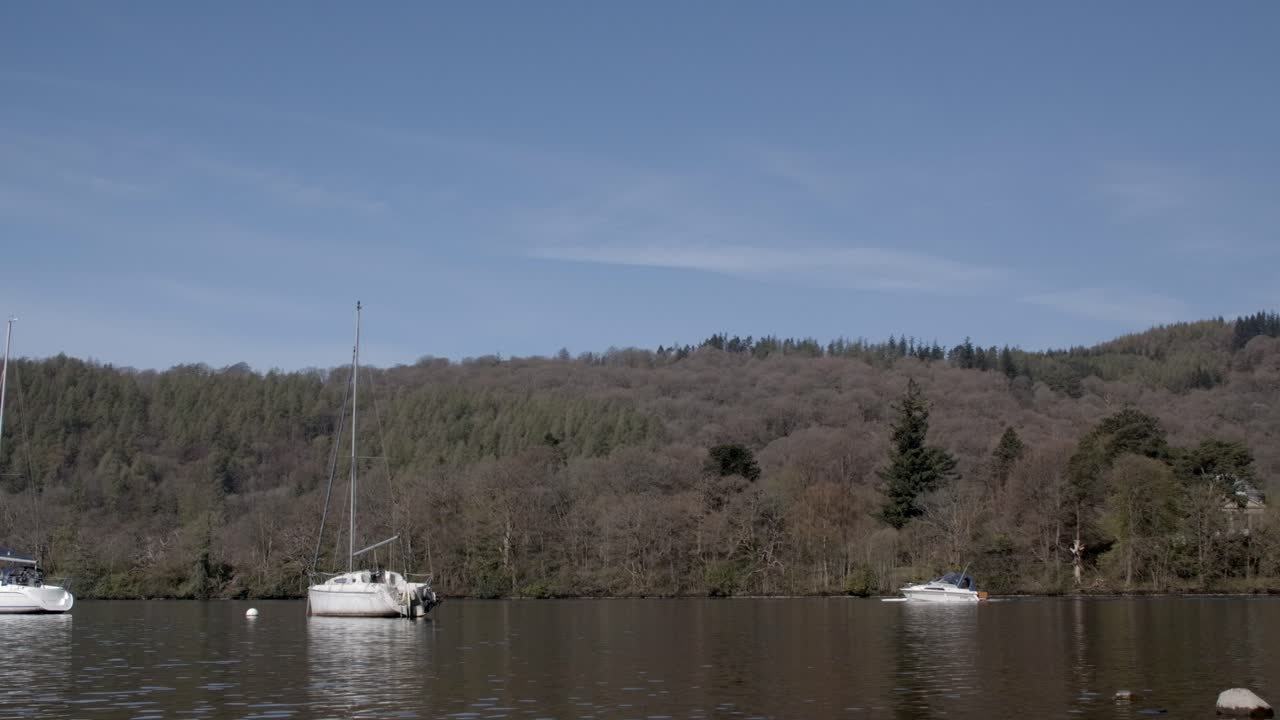 Static shot capturing a boat and kayak moving on a calm lake, surrounded by forested hills under a clear blue sky