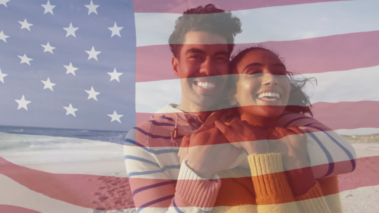 animación de la bandera de los estados unidos de américa sobre una pareja biracial abrazándose en la orilla del mar.