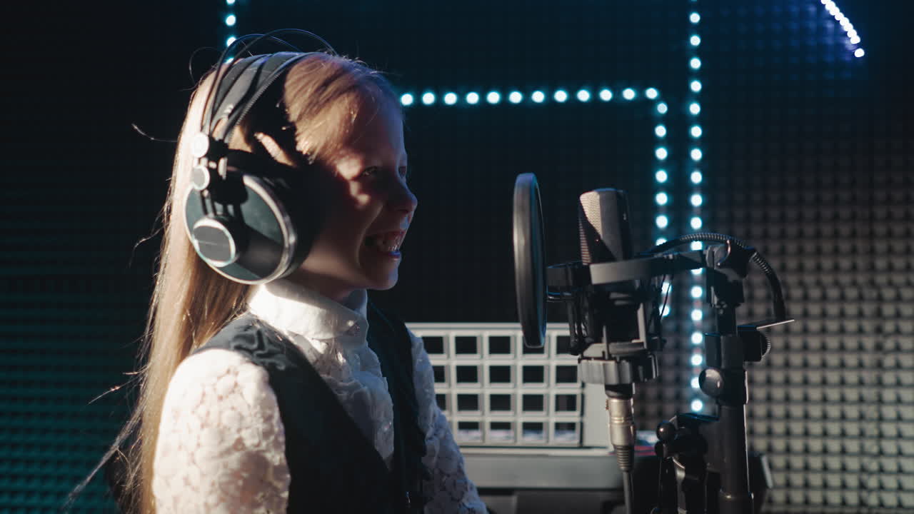 오디오 레코드 스튜디오에서 웃는 아이 행복한 어린 소녀는 단열된 방에서 전문 마이크에서 노래를 연주하기 위해 준비하는 재미를 가지고 있습니다.