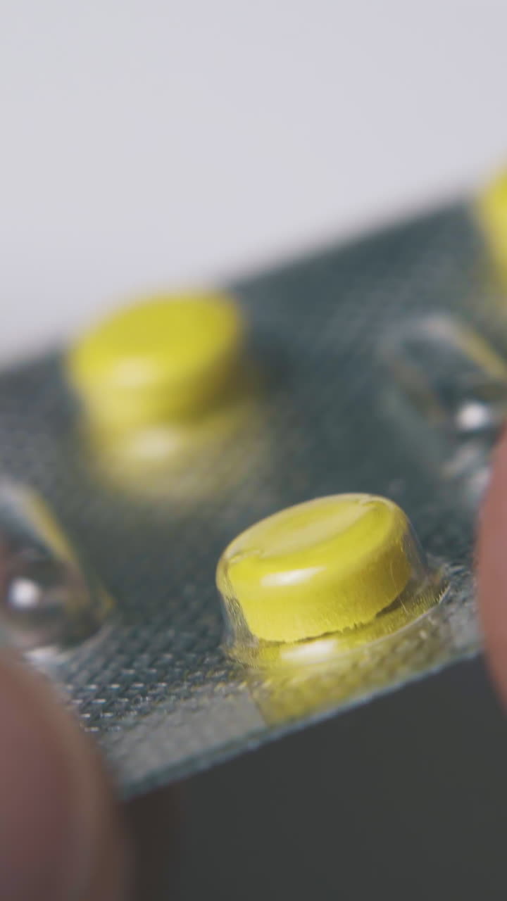 ill man holds silver blister with little yellow tablets on white background extreme close view