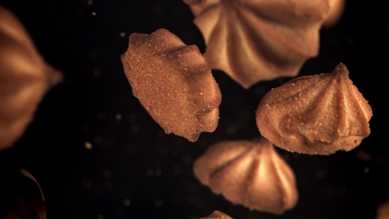Goldene Kekse schweben in Zeitlupe auf schwarzem Hintergrund