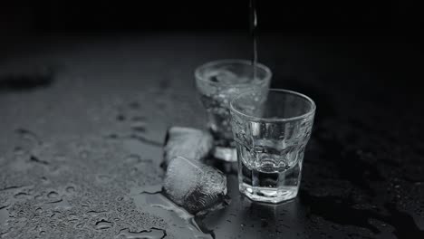 two shots of vodka with ice cubes on a black background