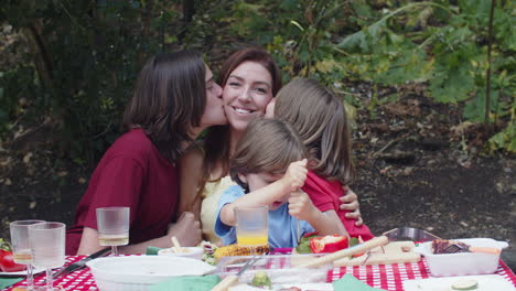 medium shot of sons sitting around mother, kissing her and then looking at the camera during a family picnic