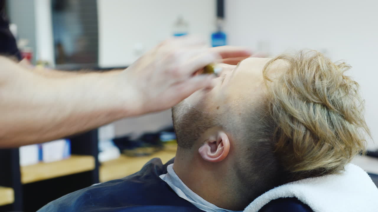 un joven se afeita con una maquinilla de afeitar peligrosa en un video hd de barbería