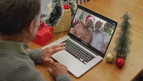 Caucasian-senior-man-on-video-call-on-laptop-with-senior-friends-at-christmas-time