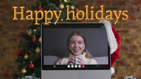 animation of happy holidays text over christmas tree and caucasian woman on laptop screen