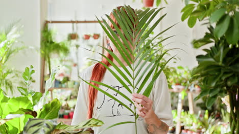 woman hiding behind a palm leaf in a plant shop