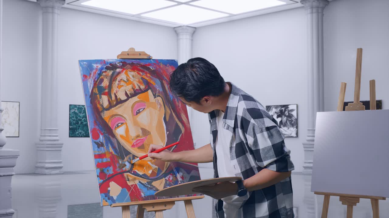 아시아 남성 예술가의 측면 뷰는 갤러리에서 오일 페인트와 브러쉬로 캔버스에 소녀를 그리는 데 집중되어 있습니다.