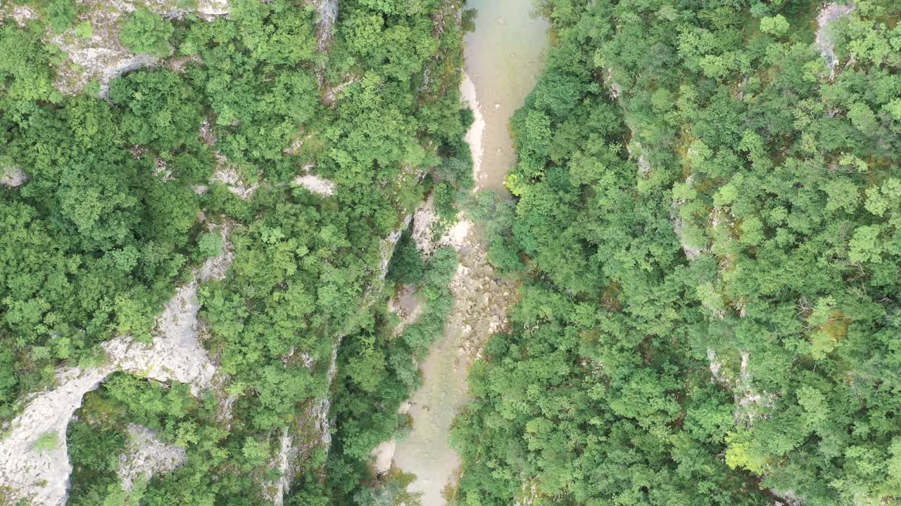 High aerial descending view above murky river in between green rocky mountains