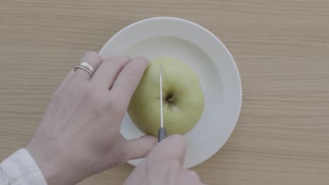 top view of woman's hands cutting green apple with knife, close up