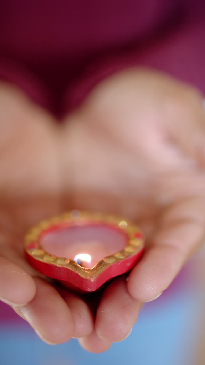 Vertical video: Holding heart-shaped candle, hands gently cupping light for diwali