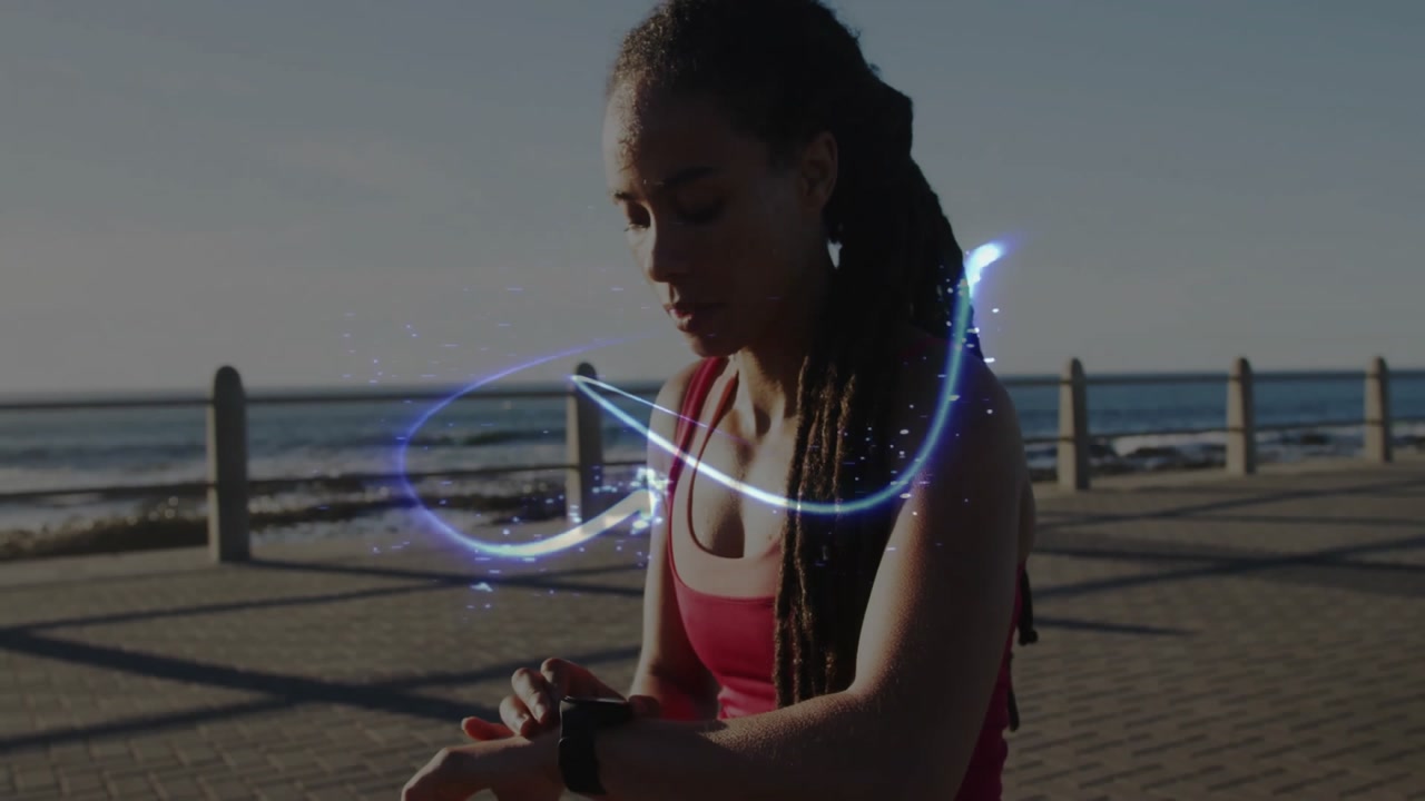 Athlete tapping smartwatch on seaside promenade activating light ribbons swirling torso for fitness