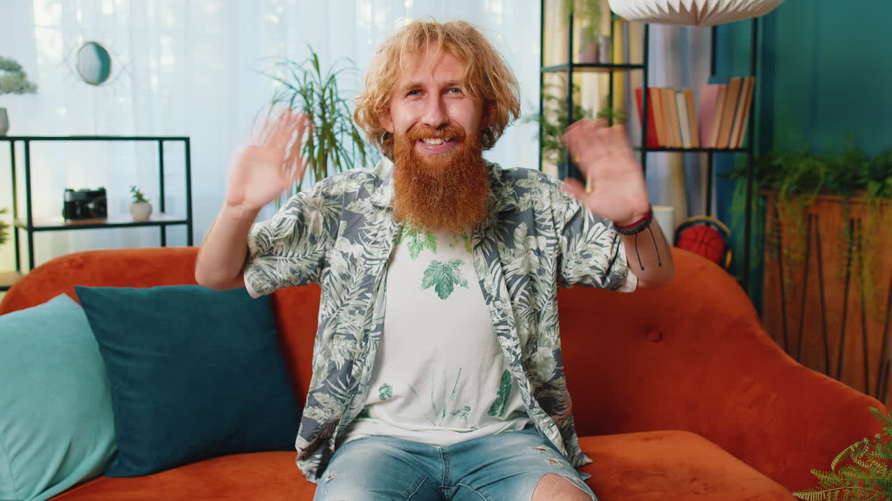 Caucasian man smiling friendly at camera waving hands gesturing hello hi greeting at home on sofa