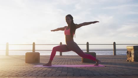 African-american-woman-in-sportswear-doing-yoga-on-promenade-by-the-sea