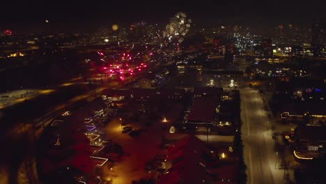 aerial view of stunning display of new year's eve fireworks lighting up city in iceland on winter night. orbiting tilt-up shot