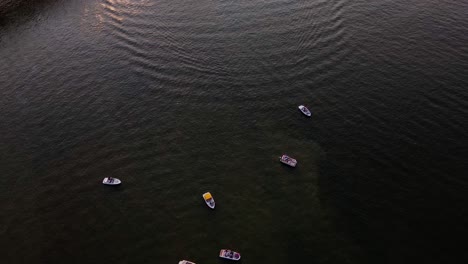 Aerial-view-over-boats-on-the-Ohio-river,-revealing-traffic-on-a-bridge-and-the-sunset-above-Jeffersonville,-USA---tilt,-drone-shot