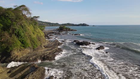 drone flying over sea waves crashing on rocks on coast of costa rica