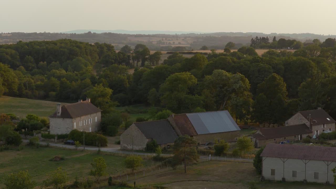 Aerial view of a countryside village with stone houses, barns, and winding roads glowing in warm sunset light