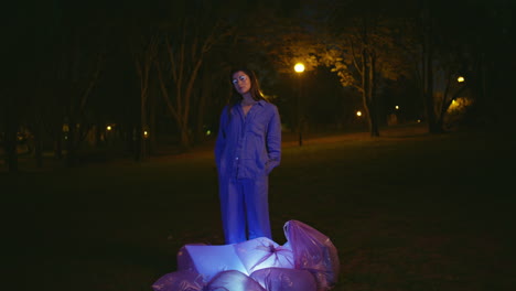 pensive girl standing night park with lantern light under glowing waste bags