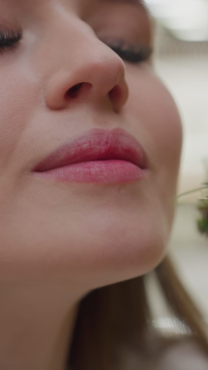 Close-up of white lady affectionately holding Christmas tree while smelling it, background features soft bokeh light effect, with unclear figure moving