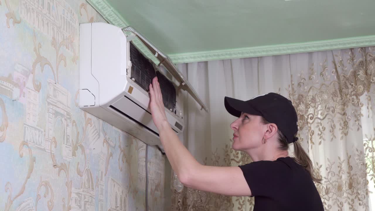 Woman from cleaning company serves household air conditioner. Inspects status of filters.