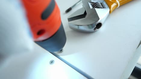 close-up of a drill screwing a screw into wood with a wrench in the background