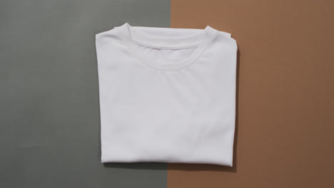 Video-of-flat-lay-of-folded-white-t-shirt-with-copy-space-on-grey-and-brown-background