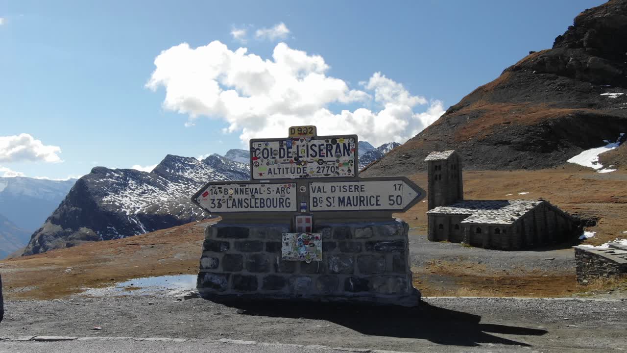 Segnale stradale del Col de l'Iseran con chiesa e catena montuosa sullo sfondo, Francia