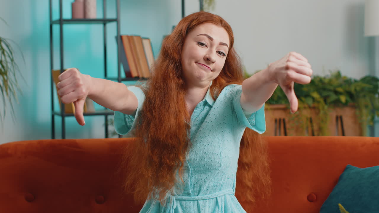 Upset young woman showing thumbs down dislike bad work disapproval dissatisfied feedback at home