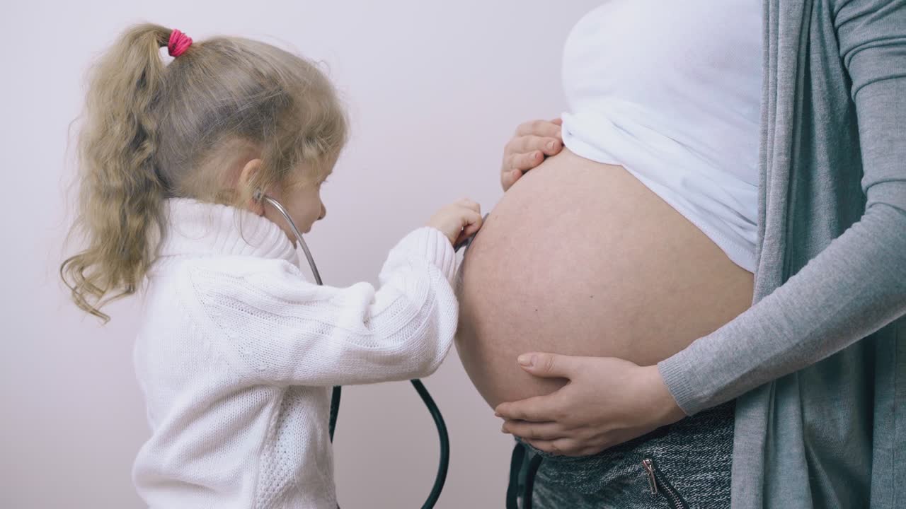 la ragazza ascolta il battito cardiaco del bambino nella pancia della madre incinta