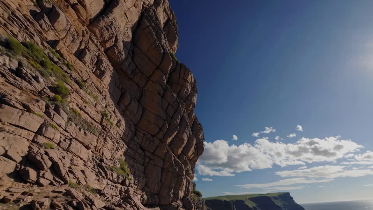 Aerial video captures rugged cliffside against a clear blue sky and ocean