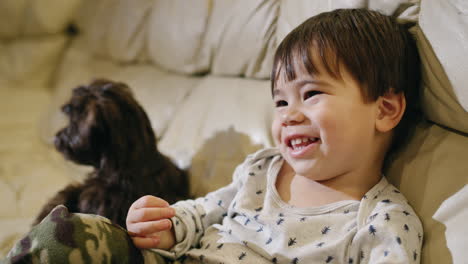 un niño asiático alegre viendo la televisión, sonriendo. un cachorro está sentado a su lado