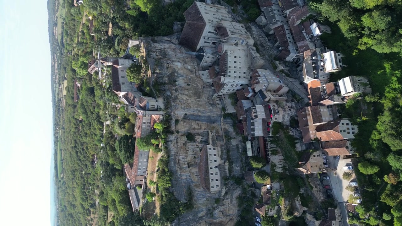 Vista aerea con drone nella campagna francese di una piccola antica città medievale su una scogliera di pietra con un castello e una cattedrale, circondata da una verde foresta montana, a Rocamadour, inquadratura verticale.