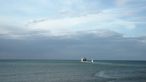 Un-Barco-Y-Un-Velero-Que-Salen-Juntos-De-La-Orilla-Y-Navegan-Lejos-En-Un-Mar-Todavía-Verde